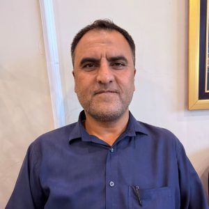 Portrait of a middle-aged man in a navy blue shirt looking at the camera, against a light interior wall.